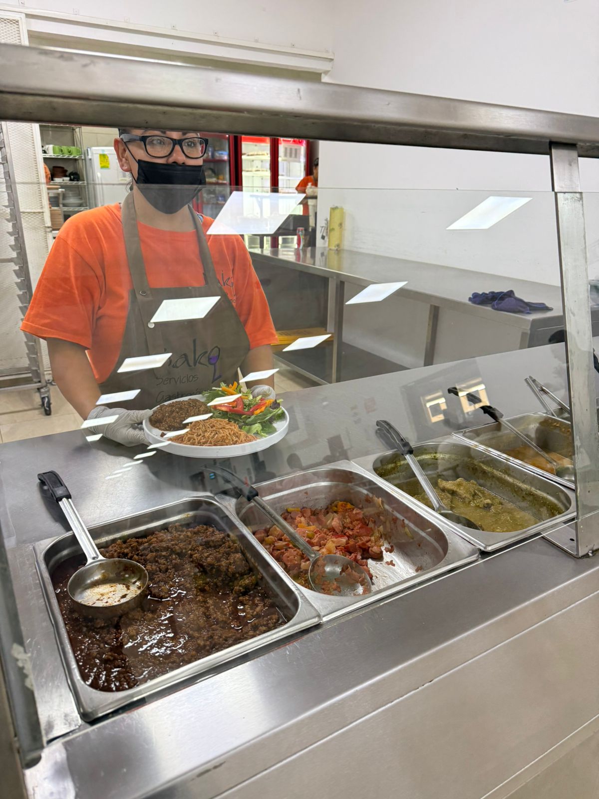 Cocinera Bako emplatando comida caliente sobre línea de servicio